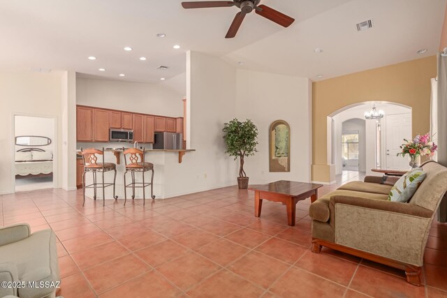 tiled living room featuring ceiling fan with notable chandelier and high vaulted ceiling