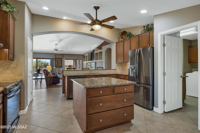 kitchen featuring sink, stainless steel appliances, a center island, kitchen peninsula, and dark stone counters