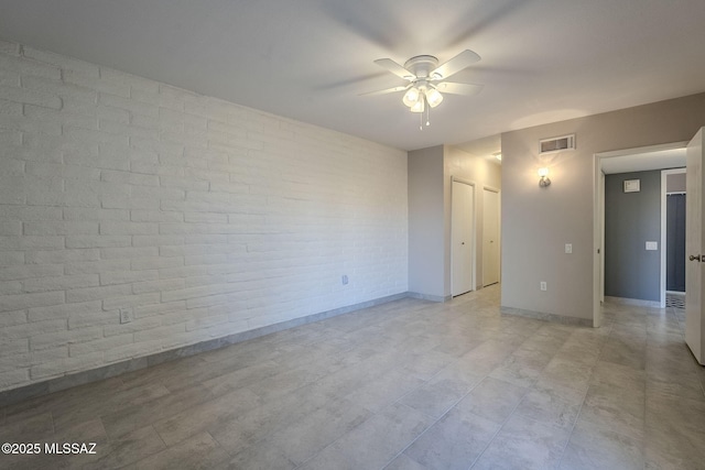 unfurnished room with ceiling fan and brick wall