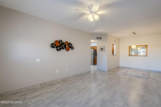 spare room with ceiling fan and brick wall