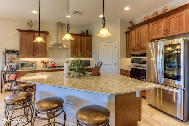 kitchen with appliances with stainless steel finishes, decorative light fixtures, a kitchen island, and wall chimney range hood