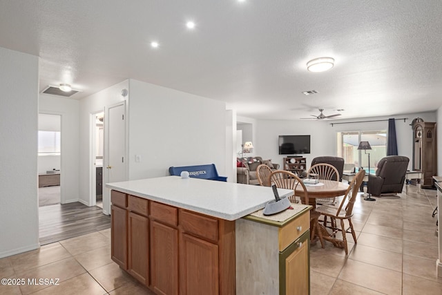 kitchen featuring light tile patterned flooring, ceiling fan, a kitchen island, and a textured ceiling