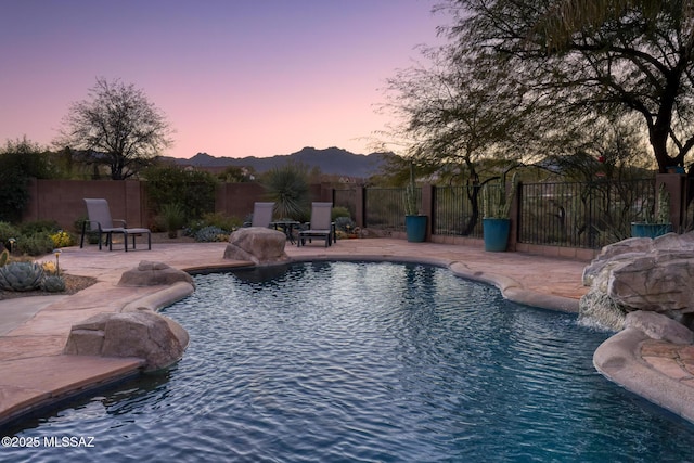 pool at dusk with a patio, pool water feature, and a mountain view