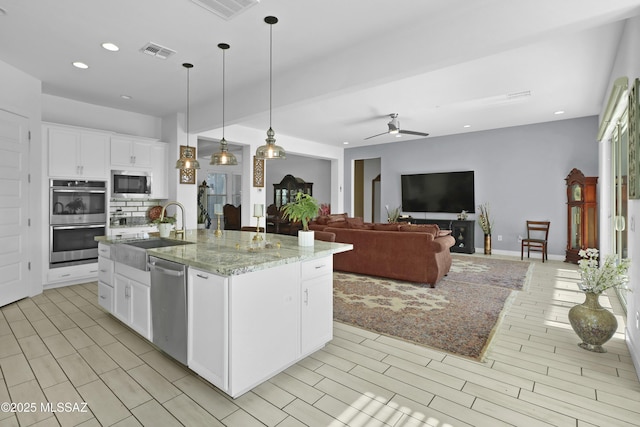 kitchen featuring appliances with stainless steel finishes, ceiling fan, sink, a center island with sink, and white cabinets