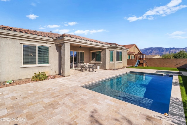 rear view of house featuring ceiling fan, a playground, a mountain view, a fenced in pool, and a patio area