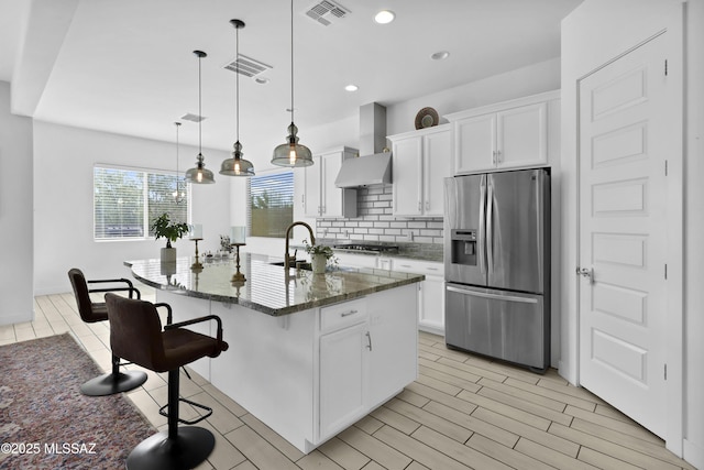 kitchen featuring wall chimney exhaust hood, white cabinetry, a kitchen island with sink, and appliances with stainless steel finishes