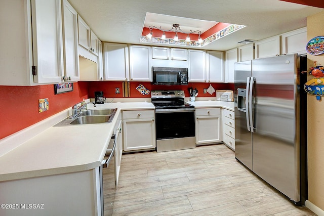 kitchen featuring white cabinets, appliances with stainless steel finishes, sink, and a tray ceiling