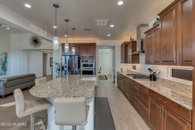 kitchen featuring appliances with stainless steel finishes, visible vents, wall chimney exhaust hood, and a kitchen bar