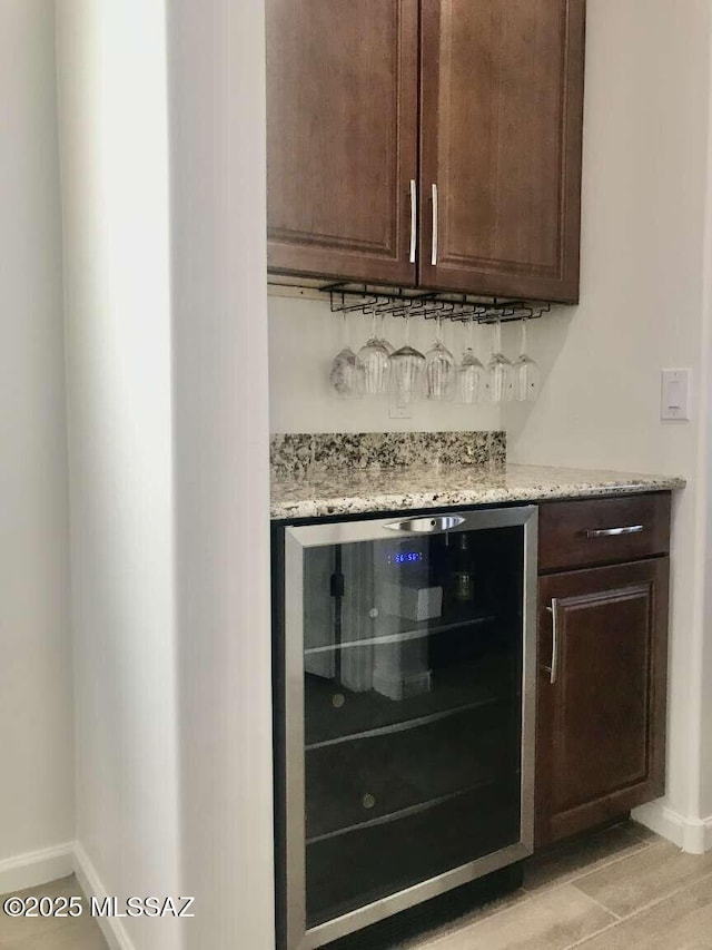 bar with a dry bar, light wood finished floors, beverage cooler, and baseboards