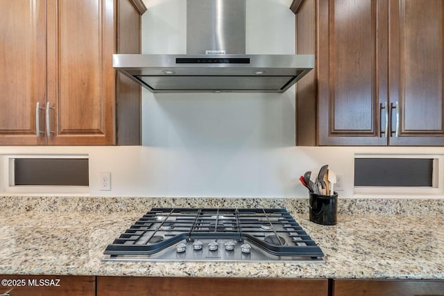 kitchen featuring wall chimney exhaust hood, stainless steel gas cooktop, and light stone counters