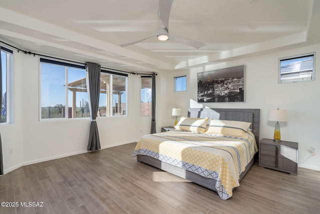 bedroom with a tray ceiling, ceiling fan, baseboards, and wood finished floors