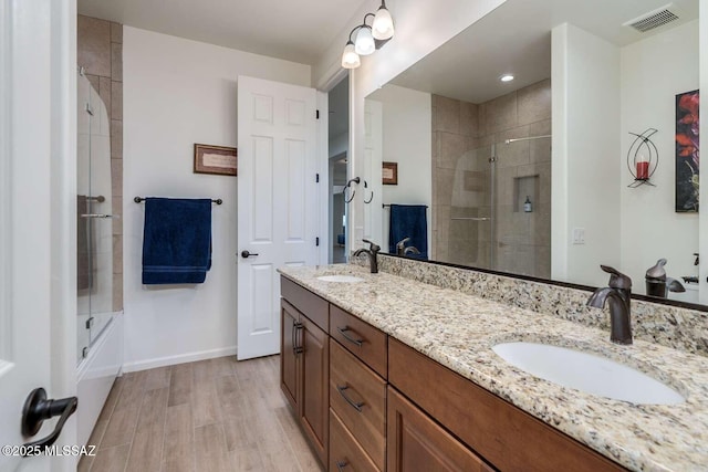 full bath with double vanity, visible vents, a sink, and wood finished floors