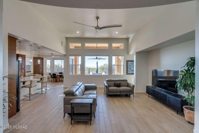 living area with light wood finished floors, ceiling fan, a high ceiling, and baseboards