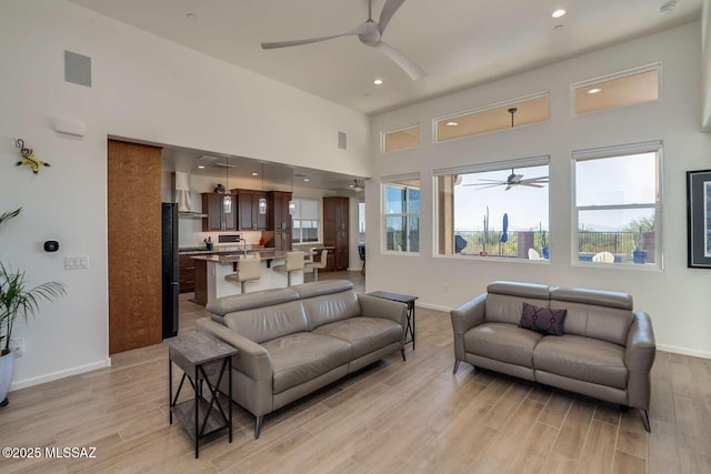 living area featuring light wood-style floors, baseboards, and a ceiling fan