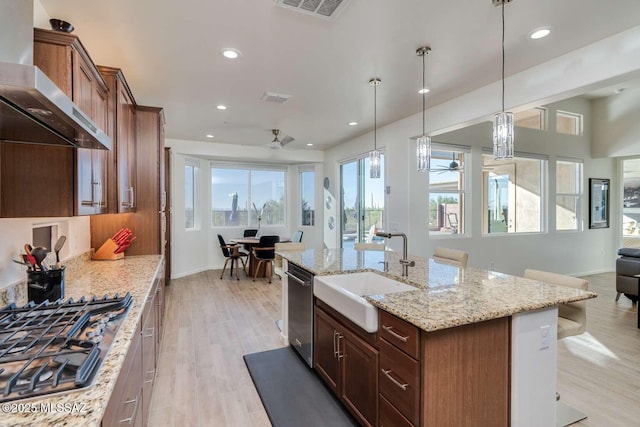 kitchen featuring light wood-style flooring, a sink, open floor plan, appliances with stainless steel finishes, and wall chimney exhaust hood