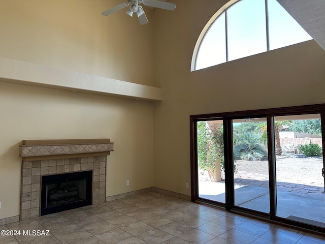 unfurnished living room with ceiling fan, a fireplace, light tile patterned floors, and a high ceiling