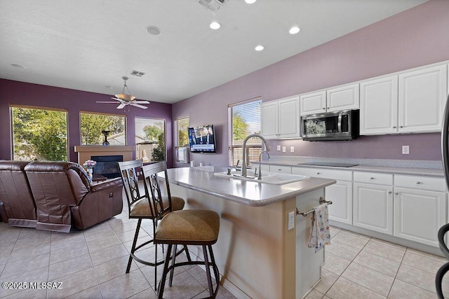 kitchen featuring sink, white cabinets, black electric stovetop, light tile patterned floors, and a center island with sink