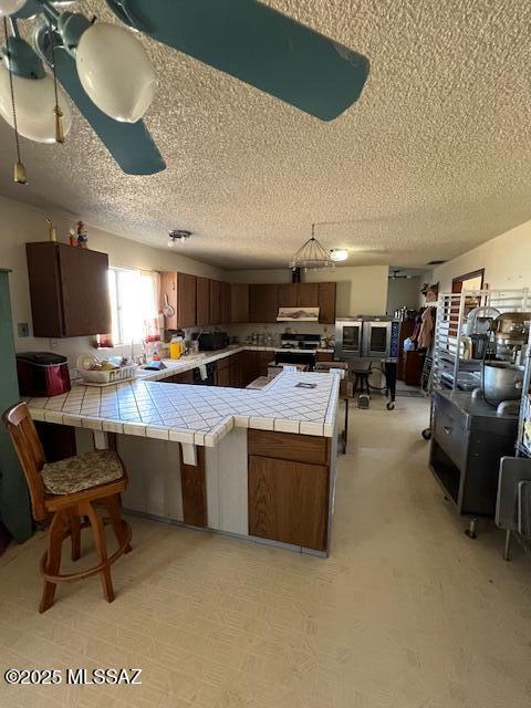 kitchen featuring range hood, tile counters, range, and kitchen peninsula