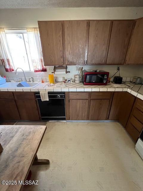 kitchen with tile countertops, black dishwasher, and sink