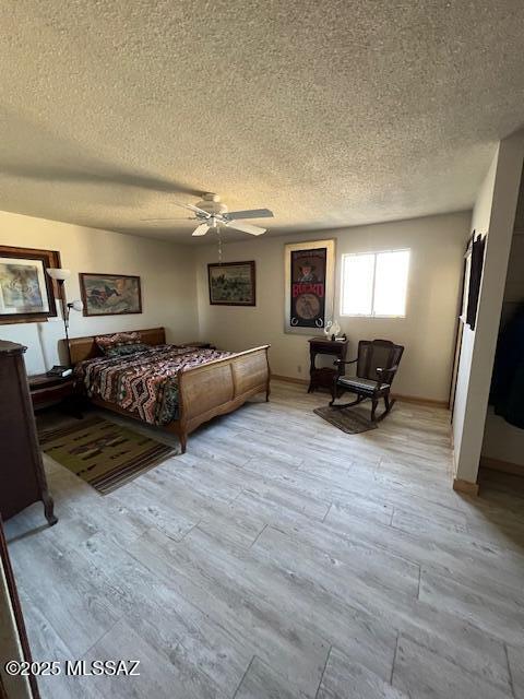 bedroom with a textured ceiling, ceiling fan, and light hardwood / wood-style floors