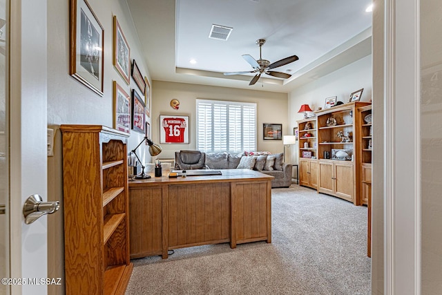 home office with ceiling fan, light colored carpet, and a tray ceiling