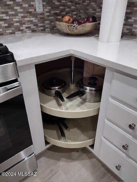 interior details with decorative backsplash, light countertops, stainless steel range with gas stovetop, and white cabinetry