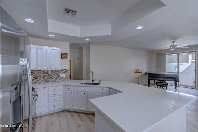 kitchen featuring visible vents, a sink, tasteful backsplash, stainless steel fridge, and a peninsula