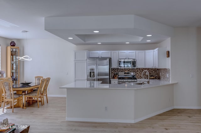 kitchen featuring light wood finished floors, a peninsula, a sink, stainless steel appliances, and backsplash