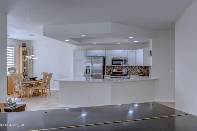 kitchen featuring tasteful backsplash, light wood-type flooring, a peninsula, white cabinets, and stainless steel appliances