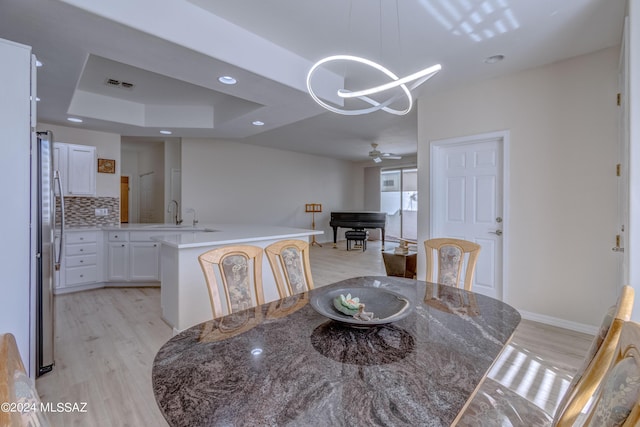 dining space with visible vents, baseboards, light wood-type flooring, ceiling fan with notable chandelier, and a raised ceiling