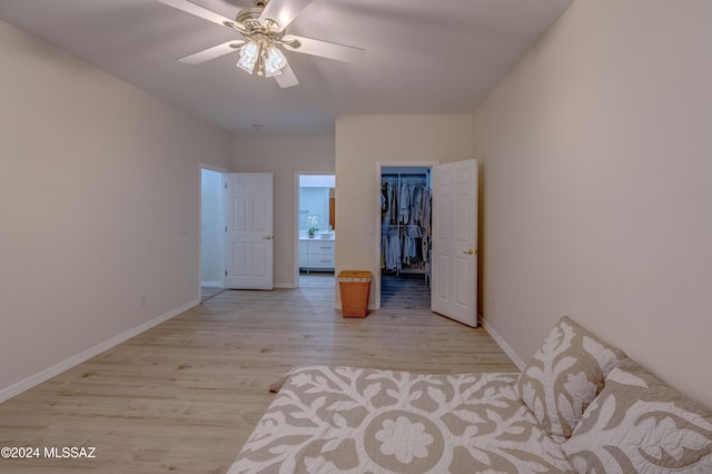 unfurnished bedroom with a walk in closet, a ceiling fan, a closet, light wood finished floors, and baseboards