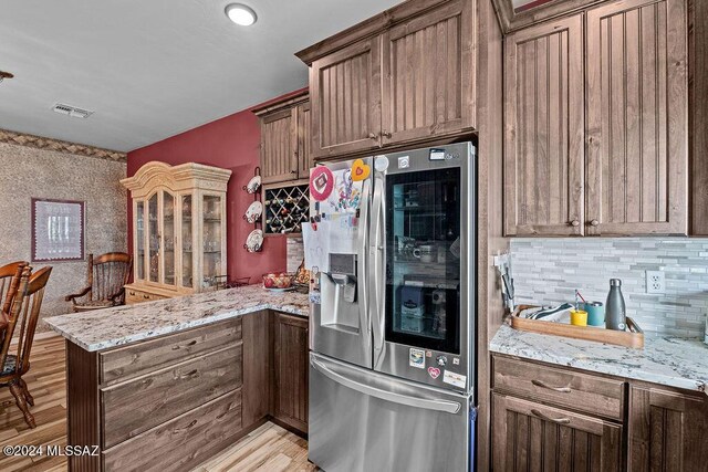 kitchen with kitchen peninsula, stainless steel fridge, decorative backsplash, and light stone countertops