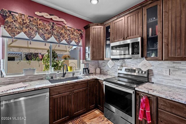 kitchen with appliances with stainless steel finishes, backsplash, light stone counters, and sink