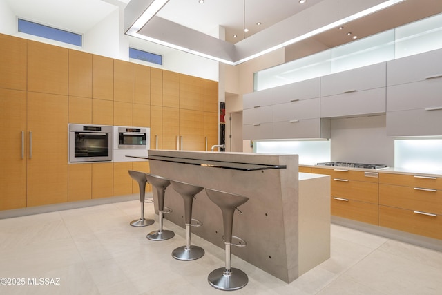 kitchen featuring a spacious island, light tile patterned floors, a high ceiling, stainless steel appliances, and white cabinets