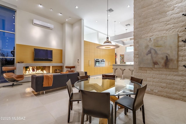 dining room featuring a wall unit AC, light tile patterned floors, a fireplace, and a high ceiling