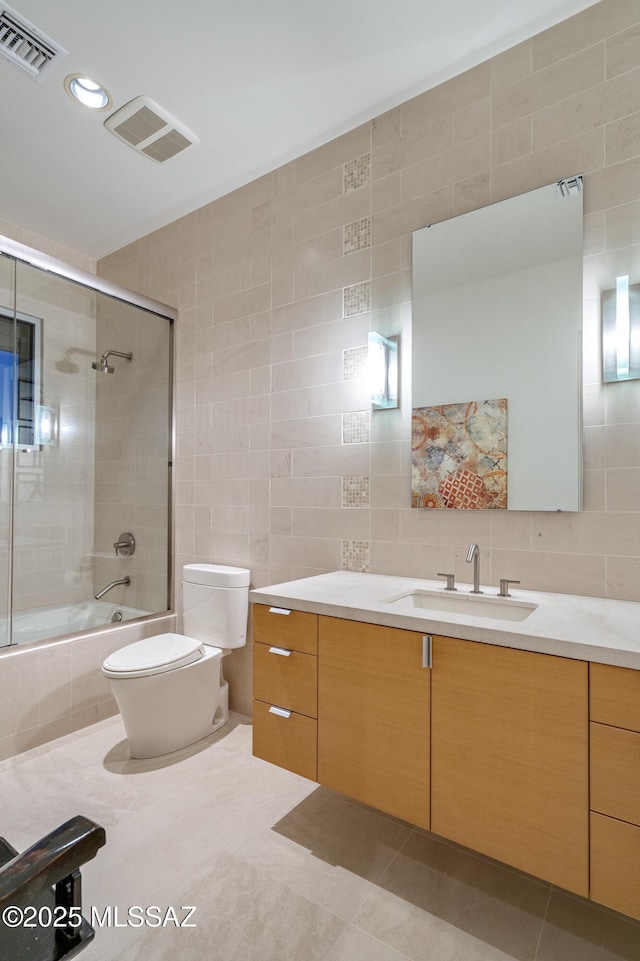 full bathroom with toilet, bath / shower combo with glass door, tile patterned flooring, tile walls, and vanity