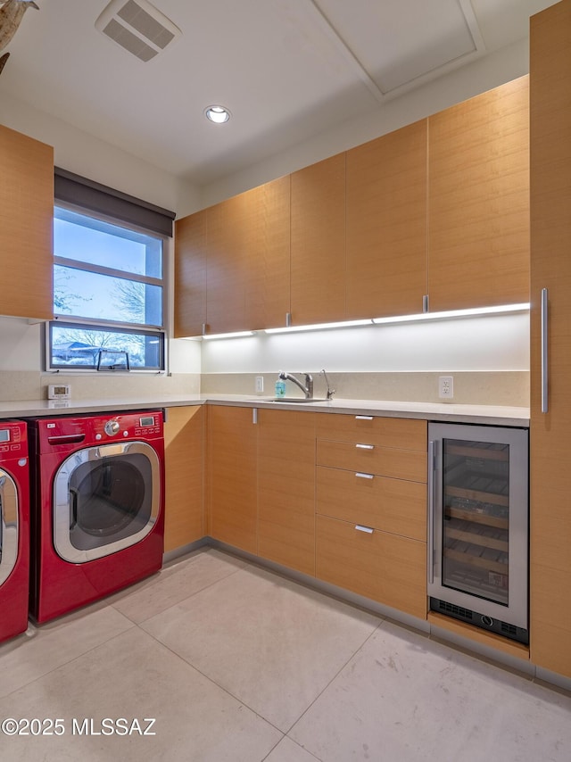 laundry area featuring light tile patterned floors, beverage cooler, washing machine and dryer, cabinets, and sink