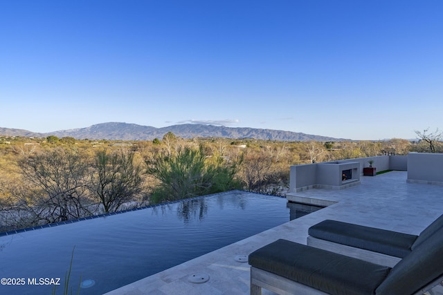 view of pool featuring exterior fireplace, a patio area, and a mountain view