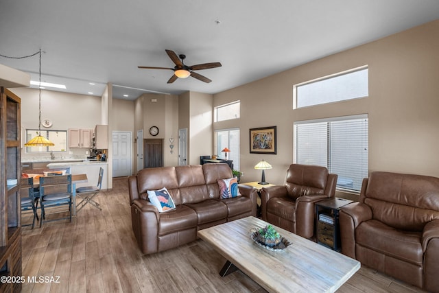 living room featuring a high ceiling, ceiling fan, and light hardwood / wood-style floors