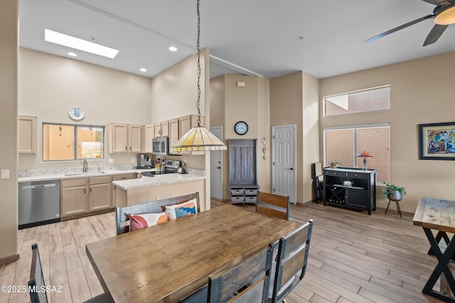 dining area with a towering ceiling, light wood-type flooring, a skylight, ceiling fan, and sink