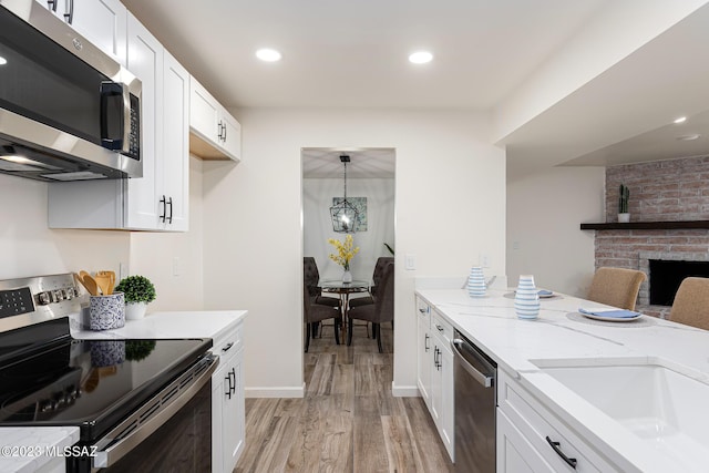 kitchen with pendant lighting, stainless steel appliances, a brick fireplace, light wood-type flooring, and white cabinetry