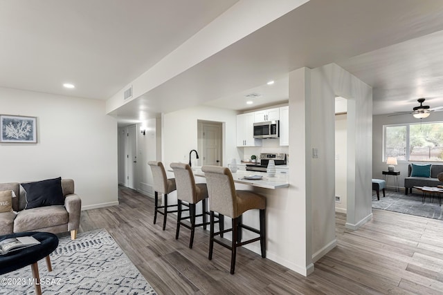 kitchen featuring stainless steel appliances, light hardwood / wood-style floors, a breakfast bar, white cabinets, and ceiling fan