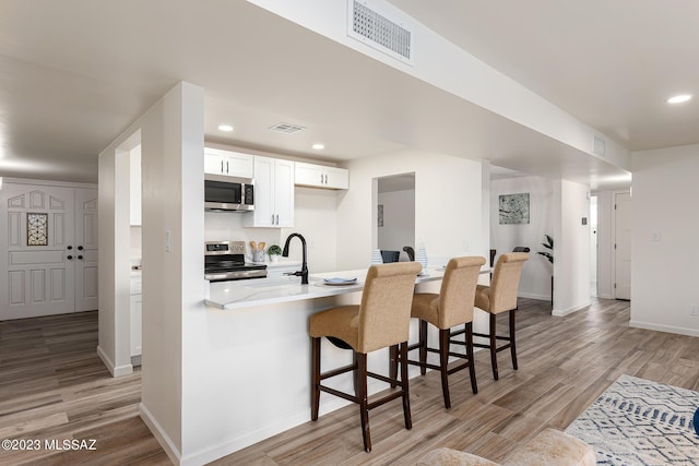 kitchen with light hardwood / wood-style flooring, stainless steel appliances, a breakfast bar area, white cabinetry, and sink