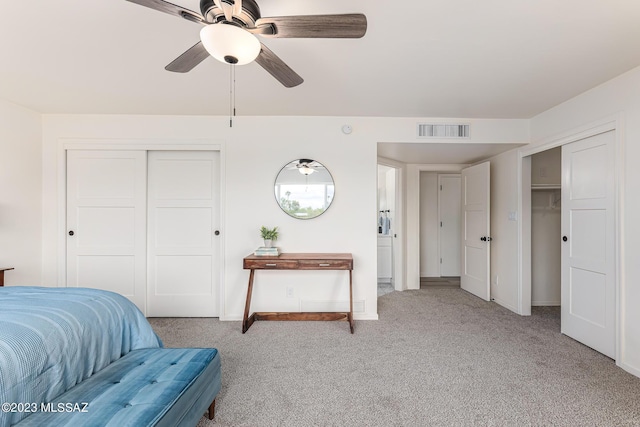 bedroom with light colored carpet, two closets, and ceiling fan