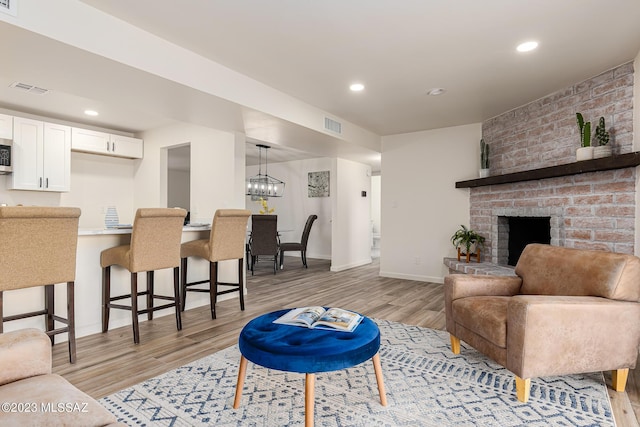 living room featuring a brick fireplace, a notable chandelier, and light hardwood / wood-style flooring