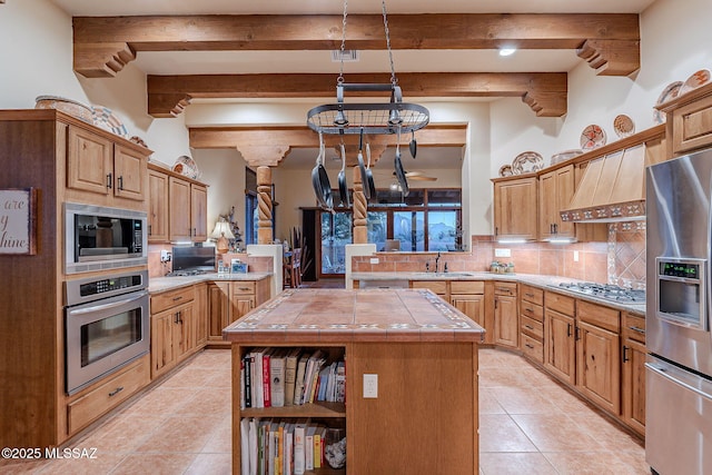 kitchen featuring a center island, decorative backsplash, appliances with stainless steel finishes, custom range hood, and tile counters