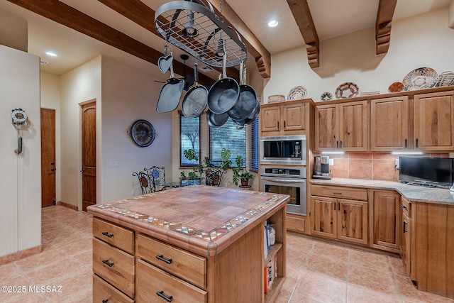 kitchen with appliances with stainless steel finishes, a center island, backsplash, tile countertops, and light tile patterned floors