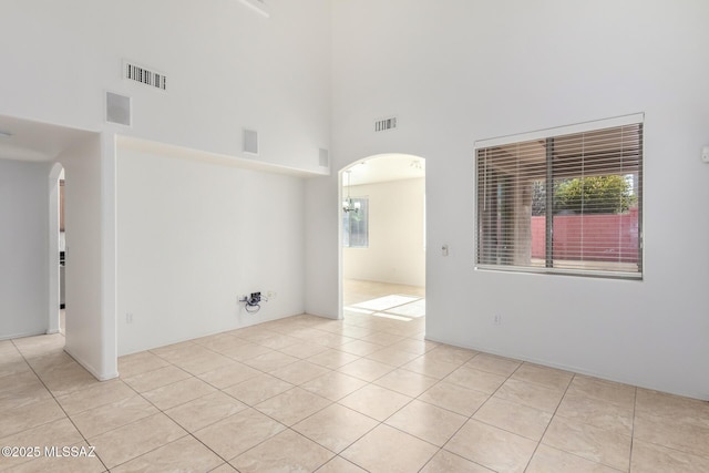 tiled spare room featuring a towering ceiling and a chandelier