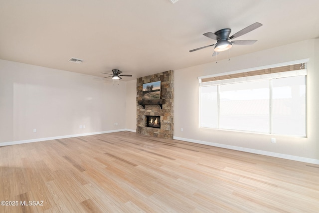 unfurnished living room with visible vents, light wood-style floors, a ceiling fan, a stone fireplace, and baseboards