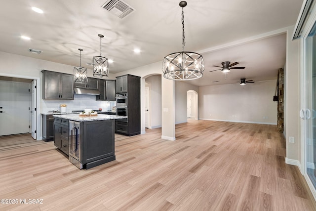 kitchen featuring decorative light fixtures, a center island, ceiling fan, light stone counters, and light hardwood / wood-style floors